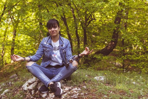 A woman meditates peacefully in a lush green forest, exuding calm and relaxation.